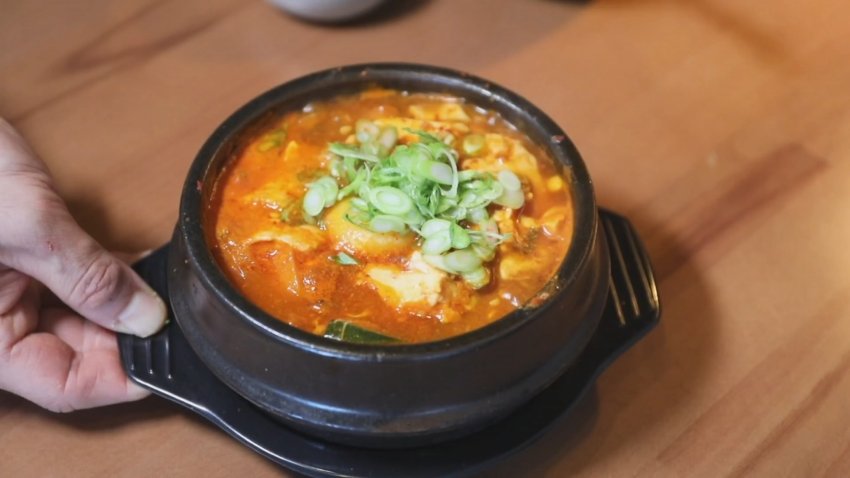A bowl of Korean food is shown, topped with green vegetables and onions.